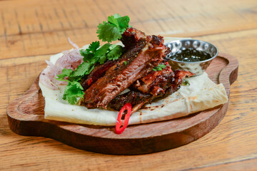 Georgian dinner. Grilled meat steak with fresh greenery served on a wooden board over rustic wooden table.