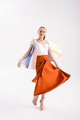 full length view of elegant woman walking with shopping bags on white