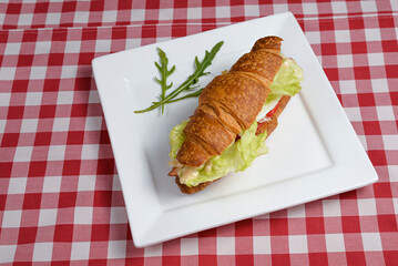 Savory croissant with tomato, letuce and cheese served on a white plate over over red plaid tablecloth.