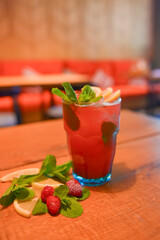 Red fruit cocktail drink with raspberry, mint and ice on dark rustic wooden table in a bar or restaurant.
