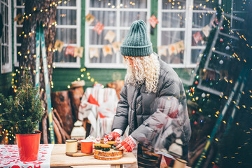 Woman decorating home for Christmas and holding small Christmas tree outside.