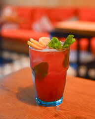 Red fruit cocktail drink with raspberry, mint and ice on dark rustic wooden table in a bar or restaurant.
