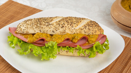 Mortadella and lettuce sandwich with oregano-covered bread, on a white plate and a bamboo mat and pepper sauce and mustard on a table with white towel, Selective focus.