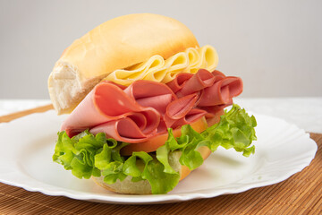 Mortadella sandwich, lettuce and cheese on a white plate and a bamboo mat with white background on a table with white towel, Selective focus. © Milton Buzon