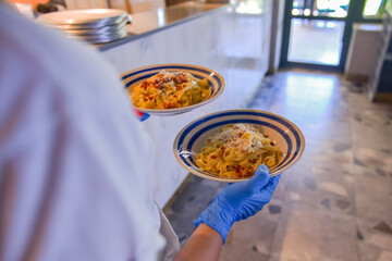 Italian pasta with sauce and parmesan cheese, served on a white oval plate. Waiter serving food at restaurant.