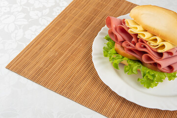 Mortadella sandwich, lettuce and cheese on a white plate and a bamboo mat with white background on a table with white towel, Selective focus. © Milton Buzon