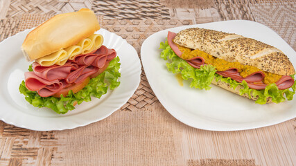 Mortadella, lettuce and cheese sandwiches and pepper and mustard sauce on white plates on a table with beige patterned tablecloth, Selective focus.
