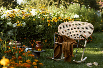 Stylish composition of countryside garden with design rattan armchair, wooden bench, plaid, food,...