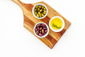 Green and black olives, olive oil in bowls on cutting board top-down
