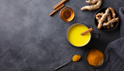 Turmeric drink, latte, tea, milk with cinnamon in a mug with fresh and powder turmeric. Dark background. Copy space. Top view.