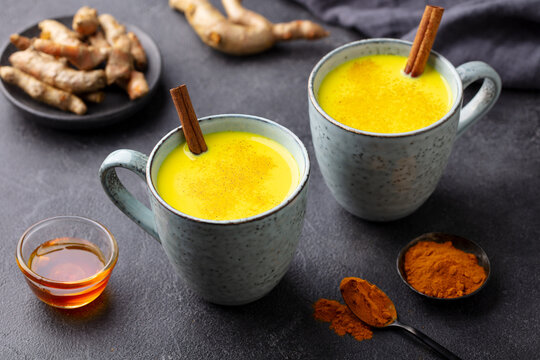 Turmeric drink, latte, tea, milk with cinnamon in a mug with fresh and powder turmeric. Grey background. Close up.