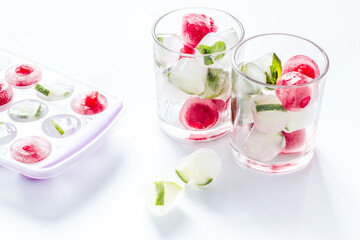 Cocktail glasses with berries in ice cubes on white table
