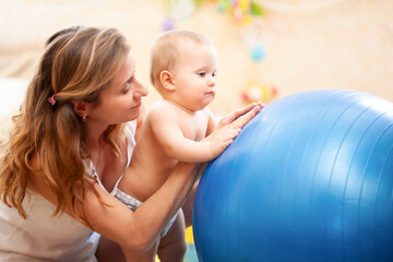 Baby playing with fitness ball with mother at home.