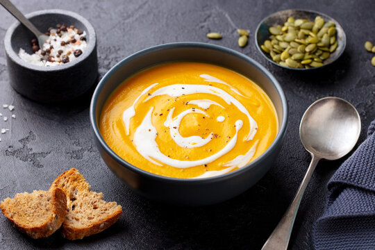 Pumpkin soup with cream in black bowl. Grey background. Close up.