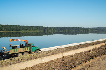 Construction of the road. The working car is on the road near the river.
