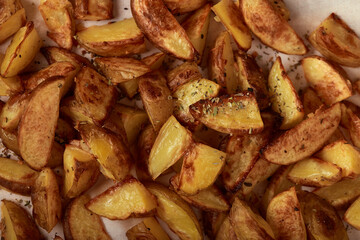 Delicious golden baked potatoes slices with seasoning on white paper
