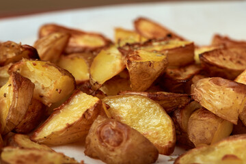 Delicious baked potatoes slices with seasoning on white paper close up from an angle