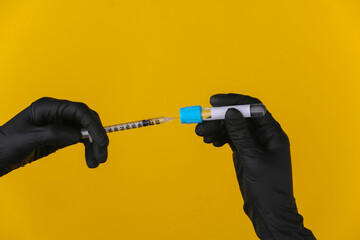 Hands in medical gloves holds a test tube with a syringe on a yellow background