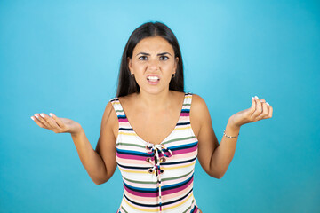 Young beautiful woman wearing swimsuit over isolated blue background clueless and confused...