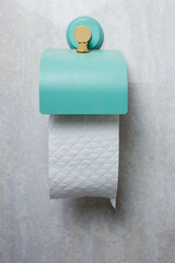 A green-blue toilet roll holder with white toilet paper on a tiled bathroom wall with space to input a text. Hygiene concept.