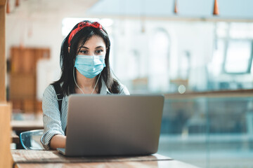 Young woman using a laptop wearing a protective face mask and studying in a university library