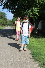 Fototapeta premium a boy and a girl go to school with masks on their faces. Social distance in the school yard. Social distance on the way to school