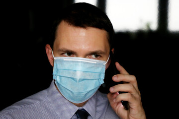Portrait of man in face mask and office clothes talking on mobile phone, smartphone in male hand close up. Concept of communication during coronavirus pandemic