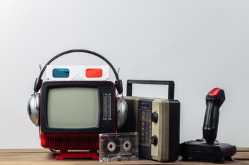 Retro portable mini tv set with headphones, 3d glasses, radio receiver, joystick, audio cassette on white background. Attributes 80s, retro style