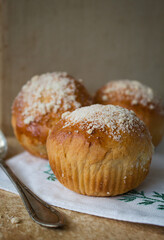 Homemade sweet petite brioche buns with pearl sugar with a spoon on the side on a white napkin on a kitchen's old table - food and drink.
