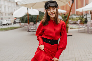 Successful attractive girl with good style walking down street. Portrait of European model in fashionable scarlet satin dress