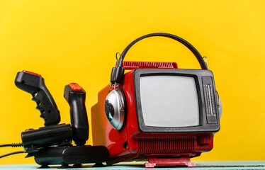 Naklejka premium Retrogaming. Video game competition. Old TV with headphones and two joysticks on yellow background. Attributes 80s