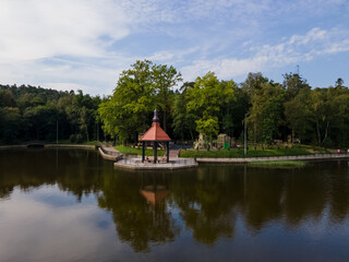 Obraz premium Gazebo on the coast of quiet lake in Svetlogorsk, green trees