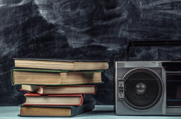 80s Retro old school portable stereo radio cassette recorder and stack of books on blackboard background.