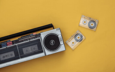 80s Retro outdated portable stereo radio cassette recorder and audio cassette on yellow background....