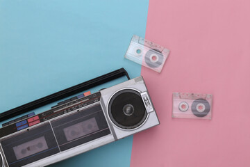 80s Retro outdated portable stereo radio cassette recorder and audio cassette on pink blue pastel background. Top view. Flat lay