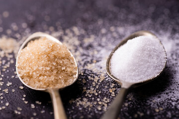 on a slate stone, in the foreground, spoons with raw and white refined cane sugar.