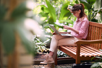 Young woman working at laptop in  botanical garden.