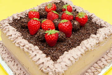 Delicious traditional Brazilian chocolate cake called Bolo de Brigadeiro with fresh strawberry topping. Isolated on yellow background. Close-up. Top view.