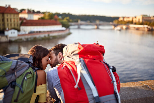 Young couple on bridge at Prague kissing at sunset.