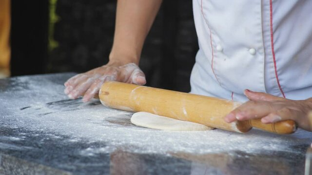 A male chef in a restaurant rolls out the dough with a rolling pin for making Focaccia