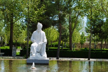 The statue of 10th century Persian poet Ferdowsi, surrounded by tall trees and water stream. Mashhad Iran - obrazy, fototapety, plakaty