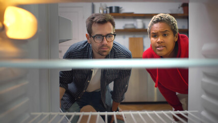 Multiethnic young couple looking into an empty refrigerator in kitchen