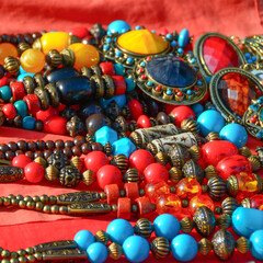 The necklace is carved from ivory, carved brass, round, with stones, stones, many colorful, handmade, tied in a beautiful necklace, arranged on a red cloth.