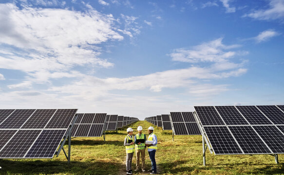 Portrait of electrician engineers in safety helmet and uniform checking solar panels. Group of three engineers at solar station.