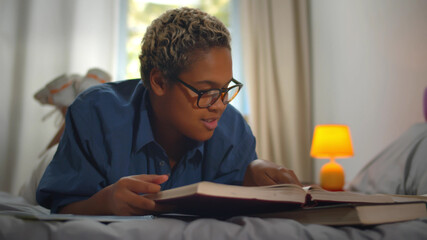 African american college student doing homework on bed at home.