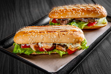 Two long submarine sandwiches with meat, cheese, bacon, tomatoes, lettuce, cucumbers and onions on...