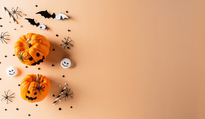 Halloween decorations made from pumpkin, paper bats and black spider on pastel orange background. Flat lay, top view with copy space for text.