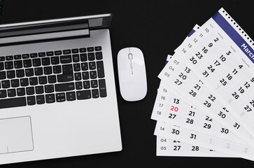 Laptop with sheets of the monthly calendar on black background. Top view