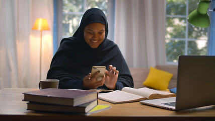 Muslim female student learning at home surfing internet on smartphone