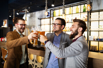 Leisure, friendship pub concept. Happy male friends drinking beer and clinking glasses at bar or pub